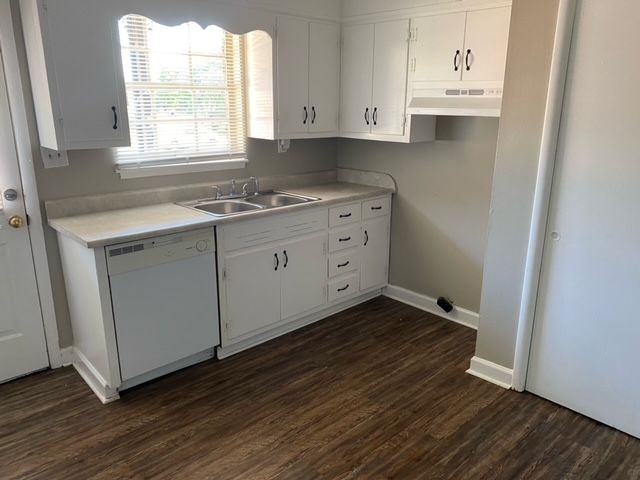 A kitchen with white cabinets , a sink , a dishwasher , and a window.