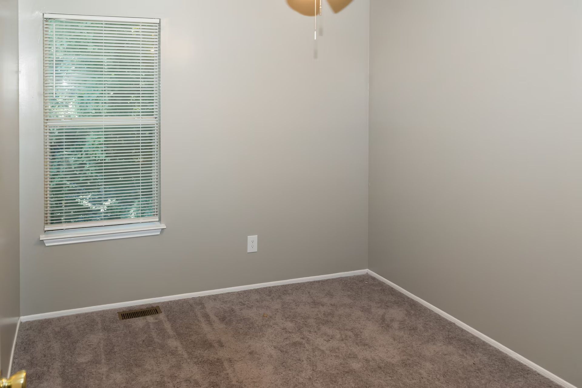 An empty bedroom with a window and a ceiling fan.