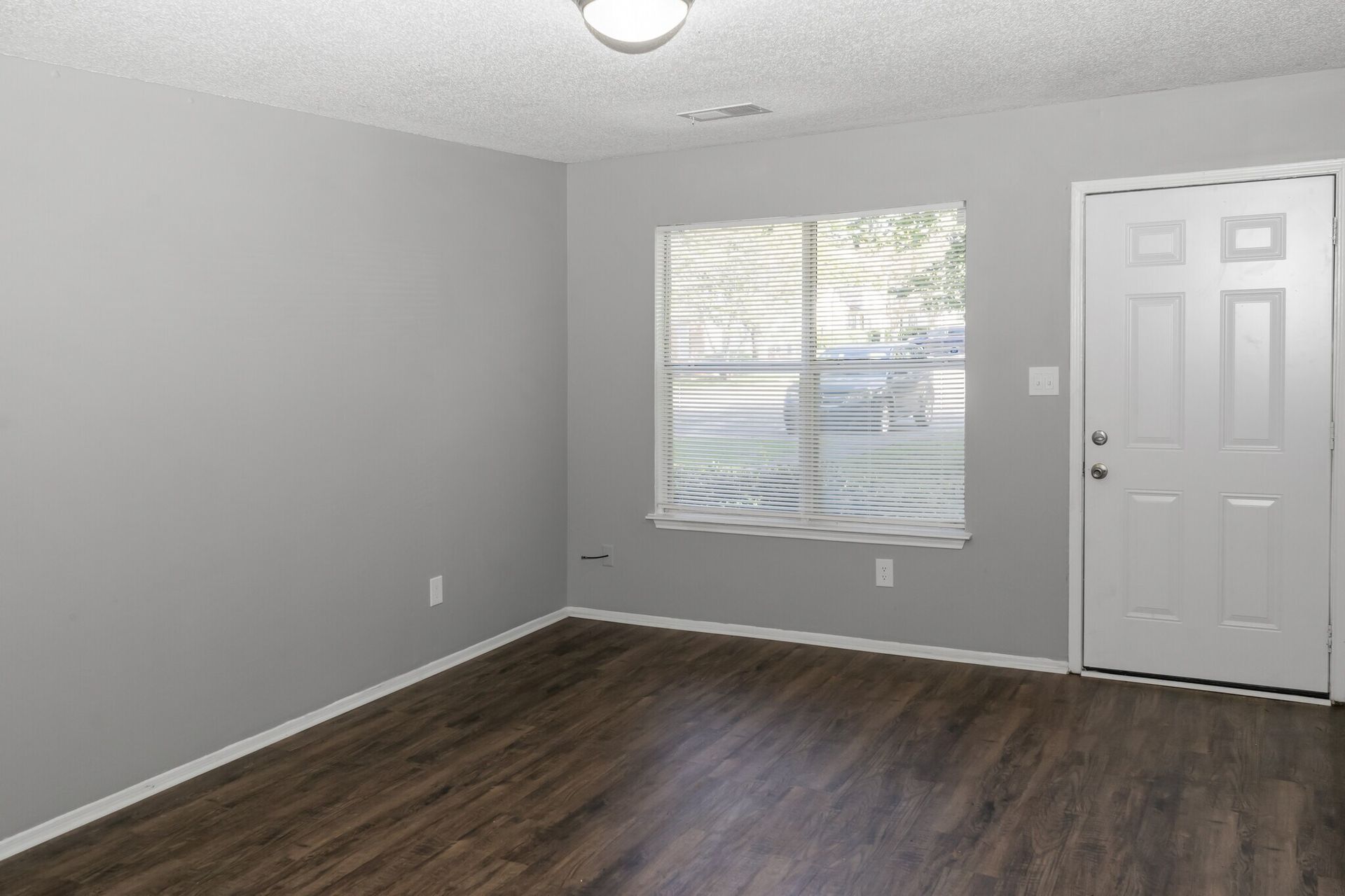 An empty living room with hardwood floors , a window and a door.