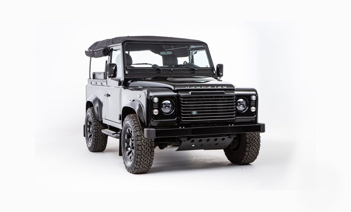 Land Rover Defender noir, capote souple, pneus tout-terrain, sur fond blanc.
