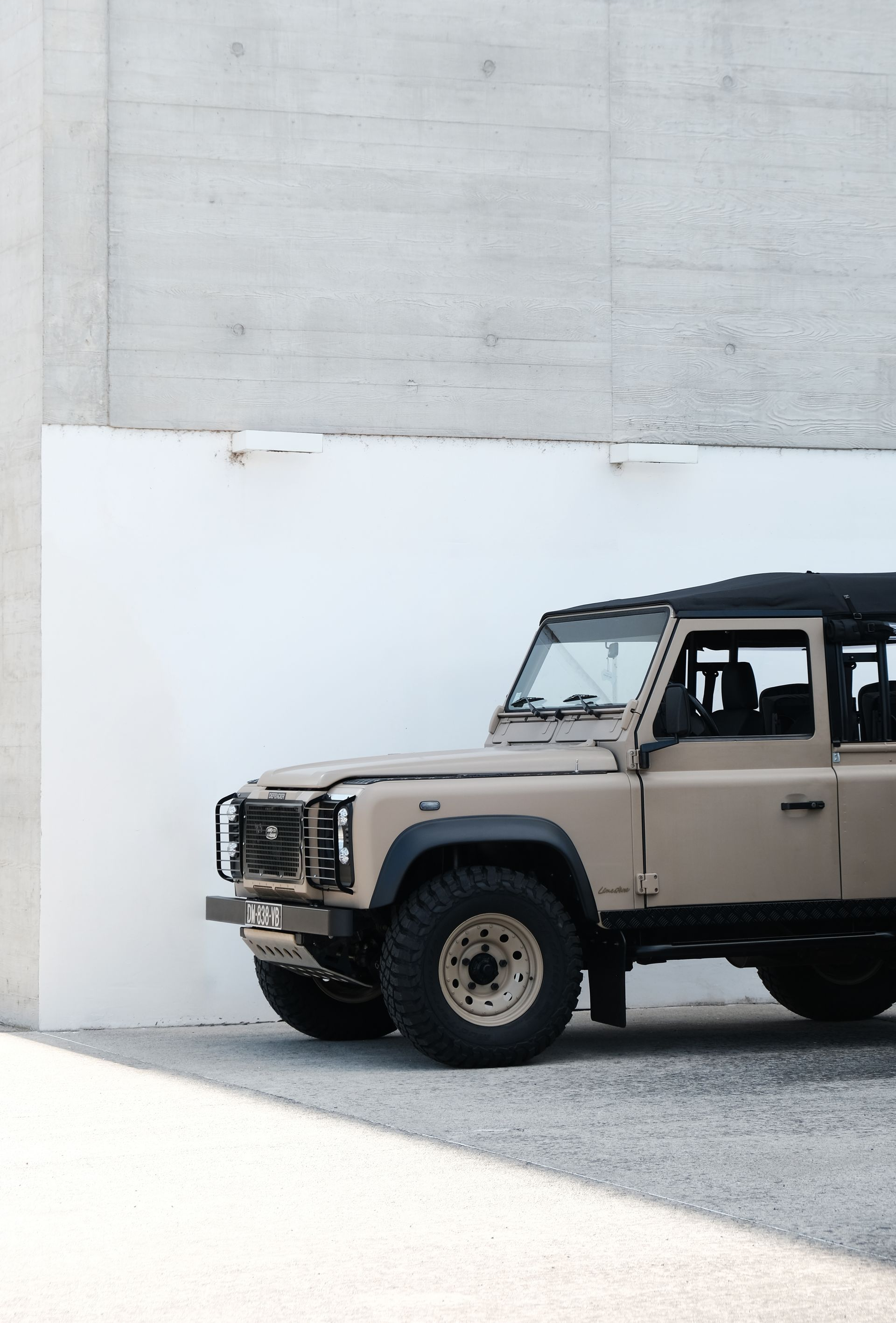 Un Land Rover Defender beige garé contre un mur en béton par une journée ensoleillée.