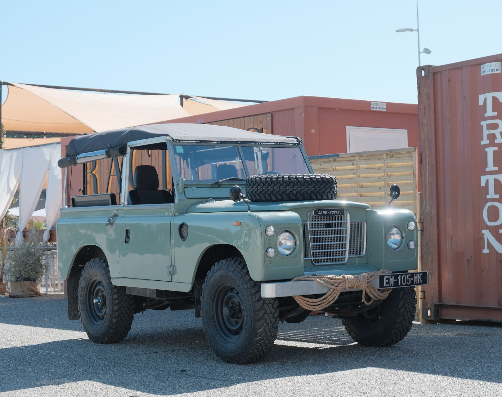 Land Rover vintage verte garée à l'extérieur avec des conteneurs de marchandises en arrière-plan.