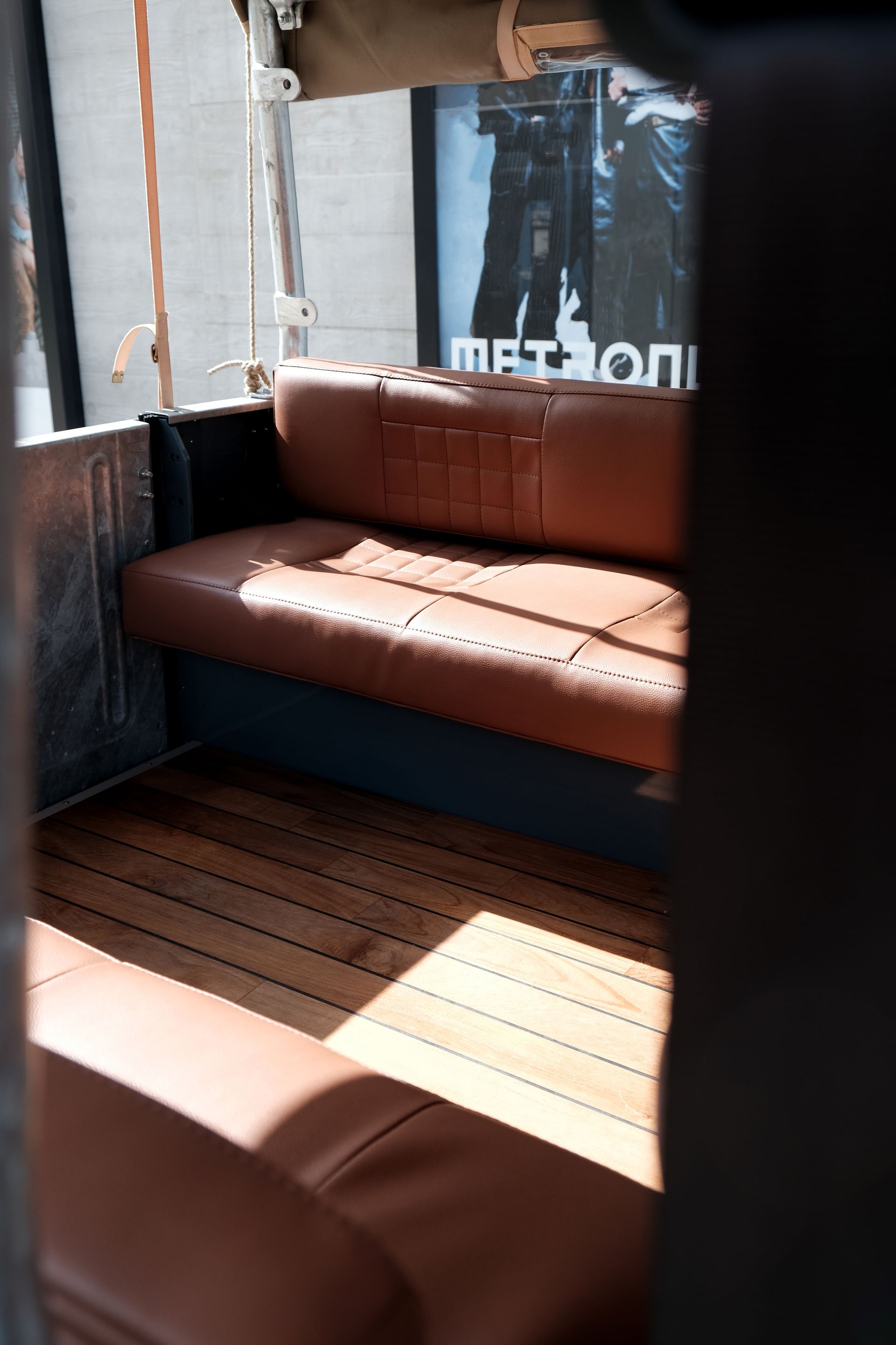 Intérieur d'un véhicule, avec banquette en cuir marron, plancher en bois et lumière du soleil qui entre en contact.