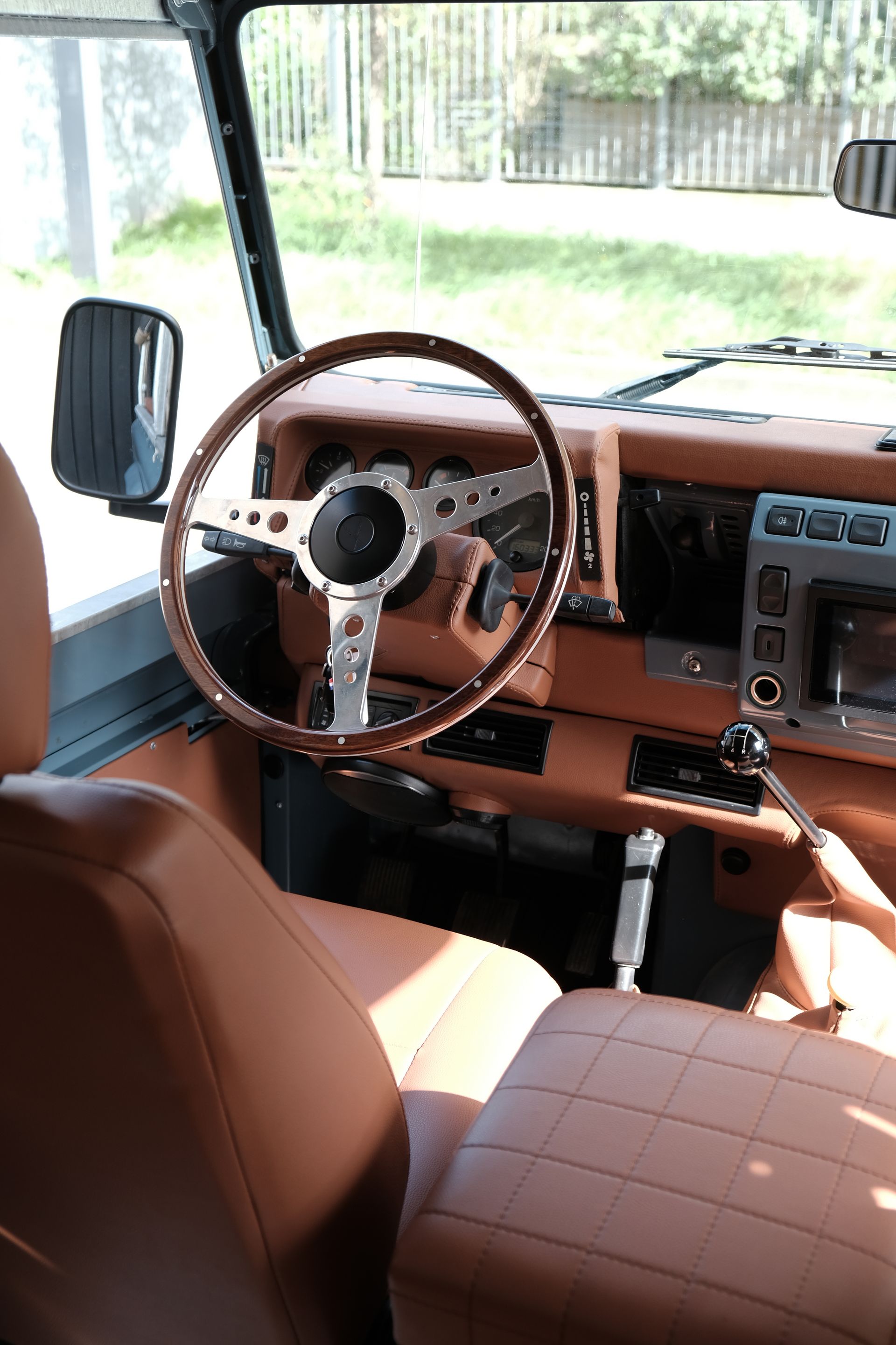 Intérieur d'un Land Rover Defender en cuir marron clair ; volant et tableau de bord en bois, accents noirs.