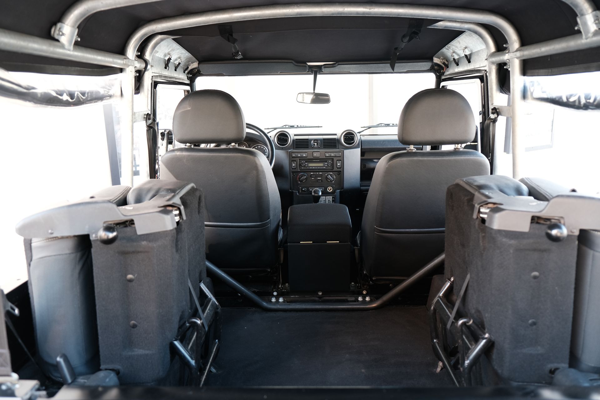 Vue intérieure d'un Land Rover Defender, montrant les sièges avant, l'arceau de sécurité et les strapontins arrière.