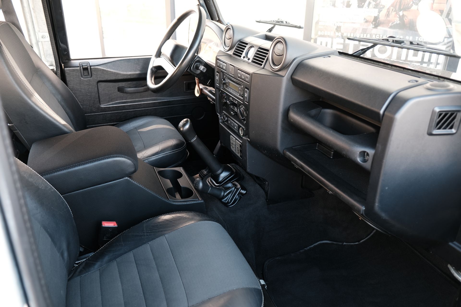 Intérieur d'un Land Rover Defender : sièges, volant, tableau de bord et console centrale noirs.