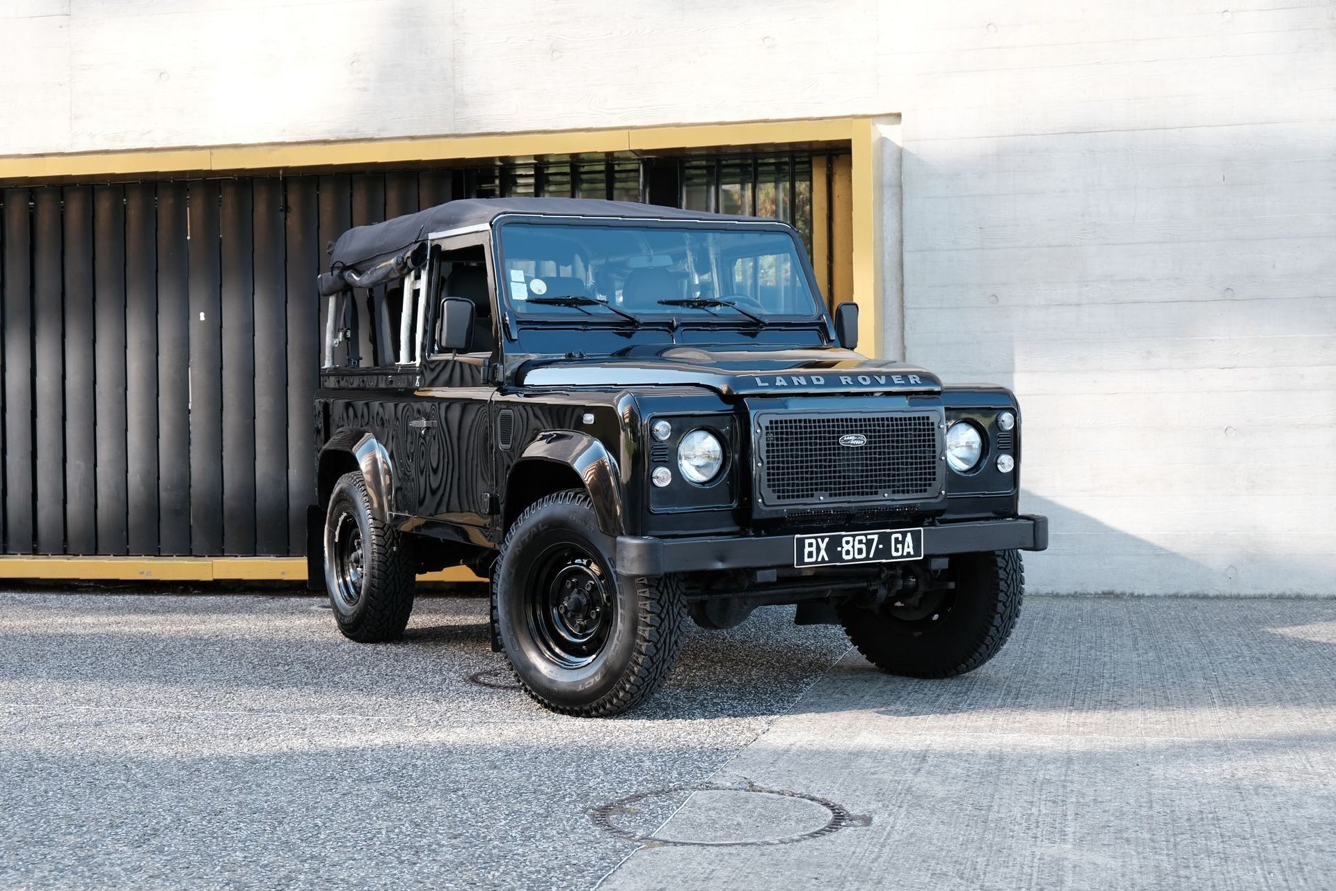 Un Land Rover Defender noir est garé devant un bâtiment.