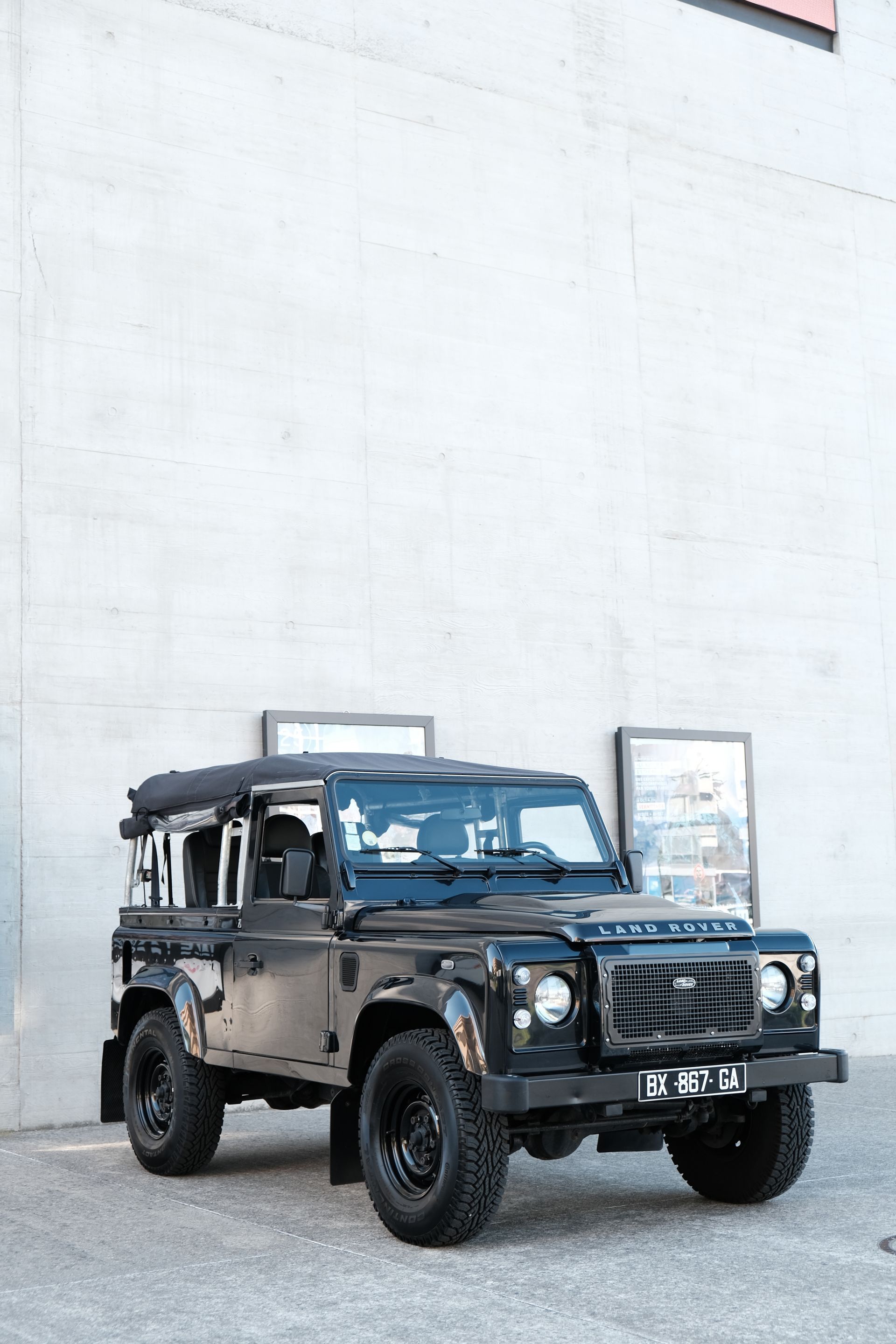 Un Land Rover Defender noir est garé devant un mur en béton.