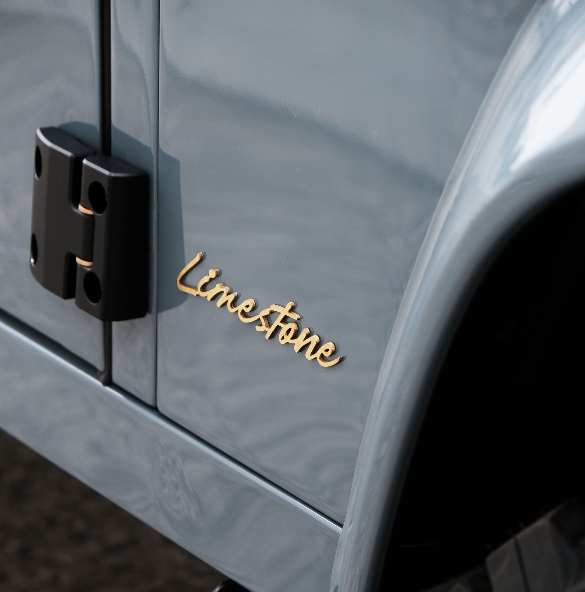 Gros plan sur une portière de voiture bleu-gris avec l'inscription « Limestone » en lettres dorées. Une charnière noire est visible.