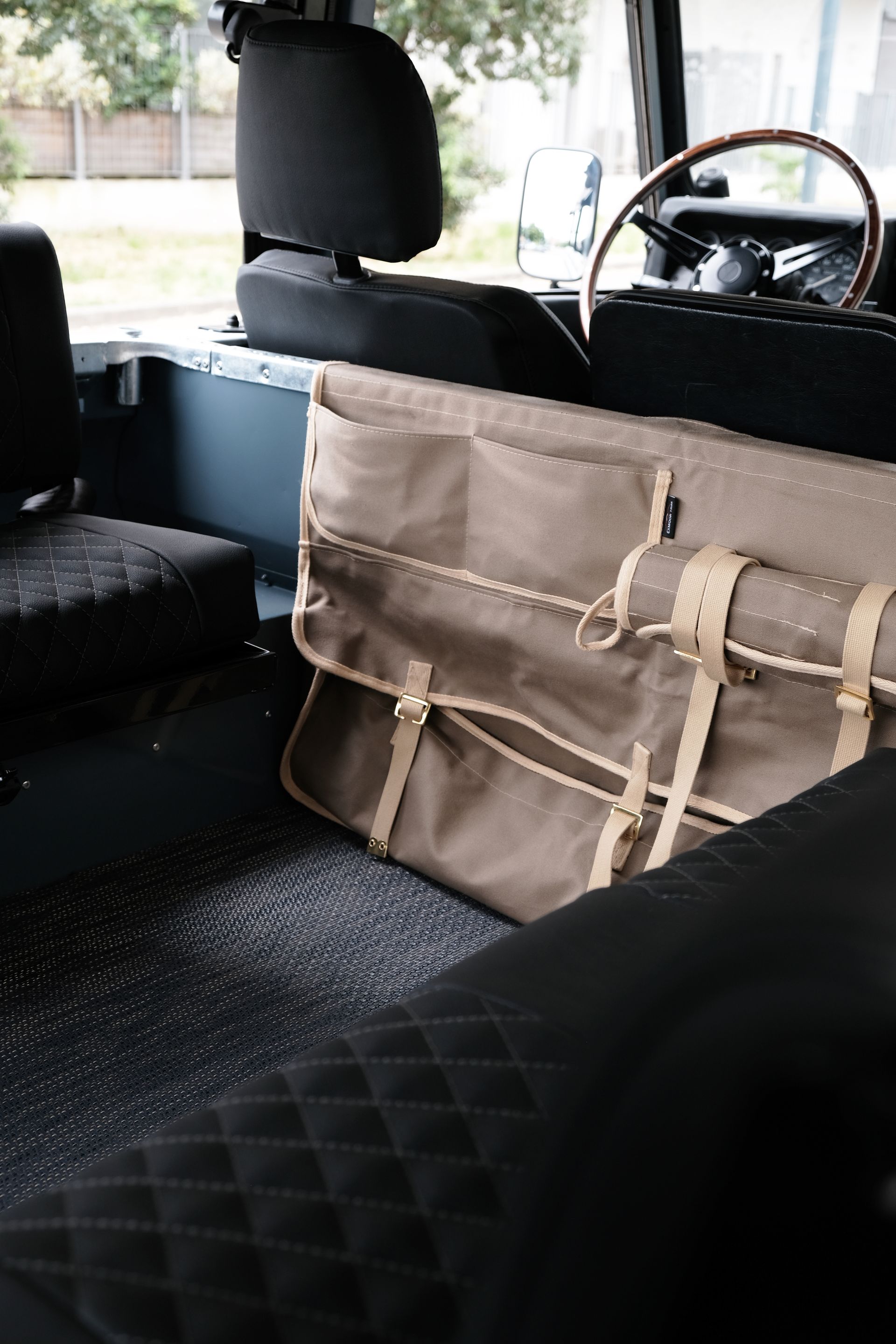 À l'intérieur du véhicule, un sac beige est posé derrière un siège noir. Intérieur noir, volant en bois visible.