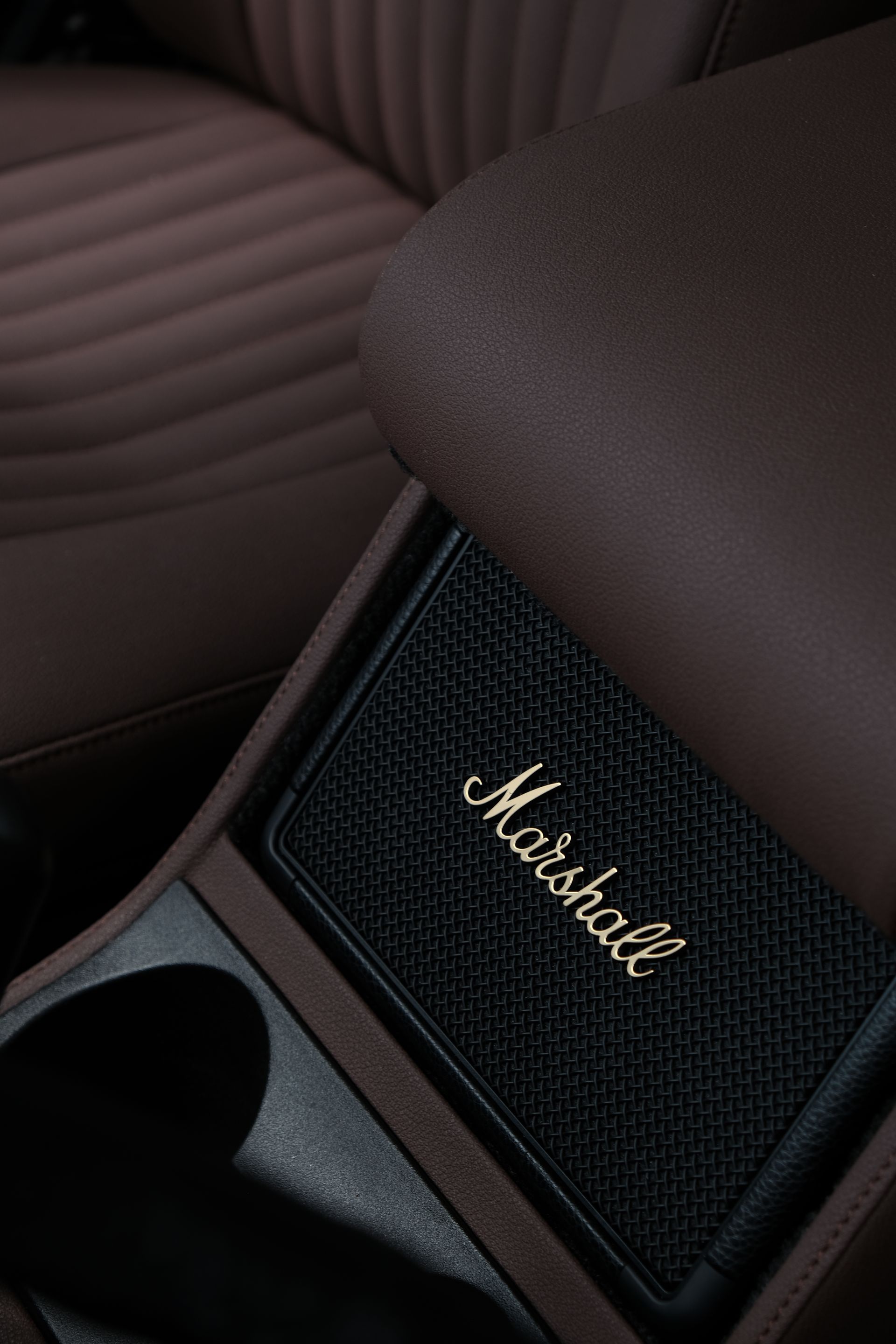 Gros plan sur la console centrale d'une voiture, avec un haut-parleur Marshall à logo doré, un intérieur en cuir marron et des porte-gobelets.