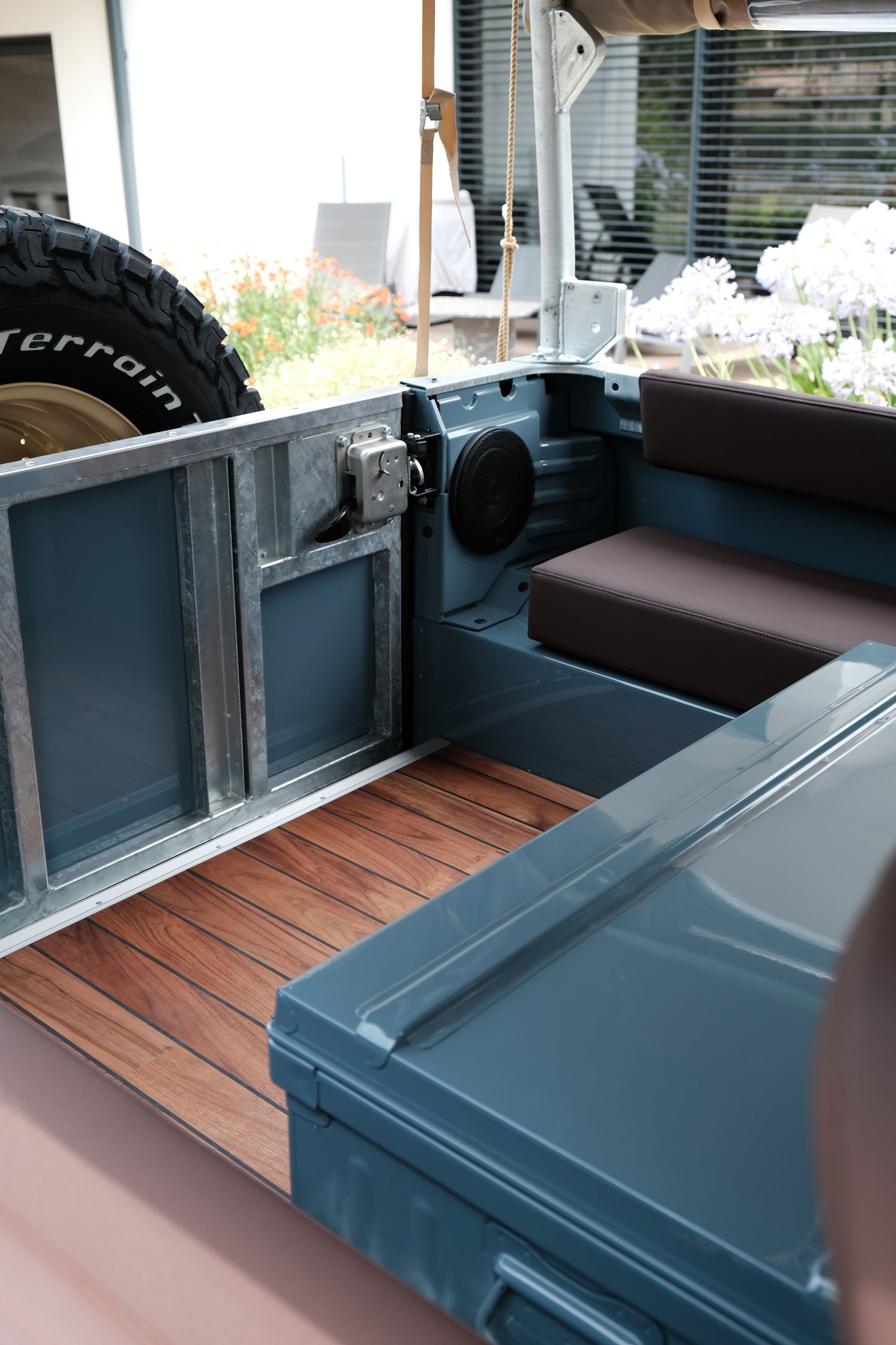 Vue intérieure d'un Land Rover turquoise avec plancher en bois et banquette marron, roue de secours visible.