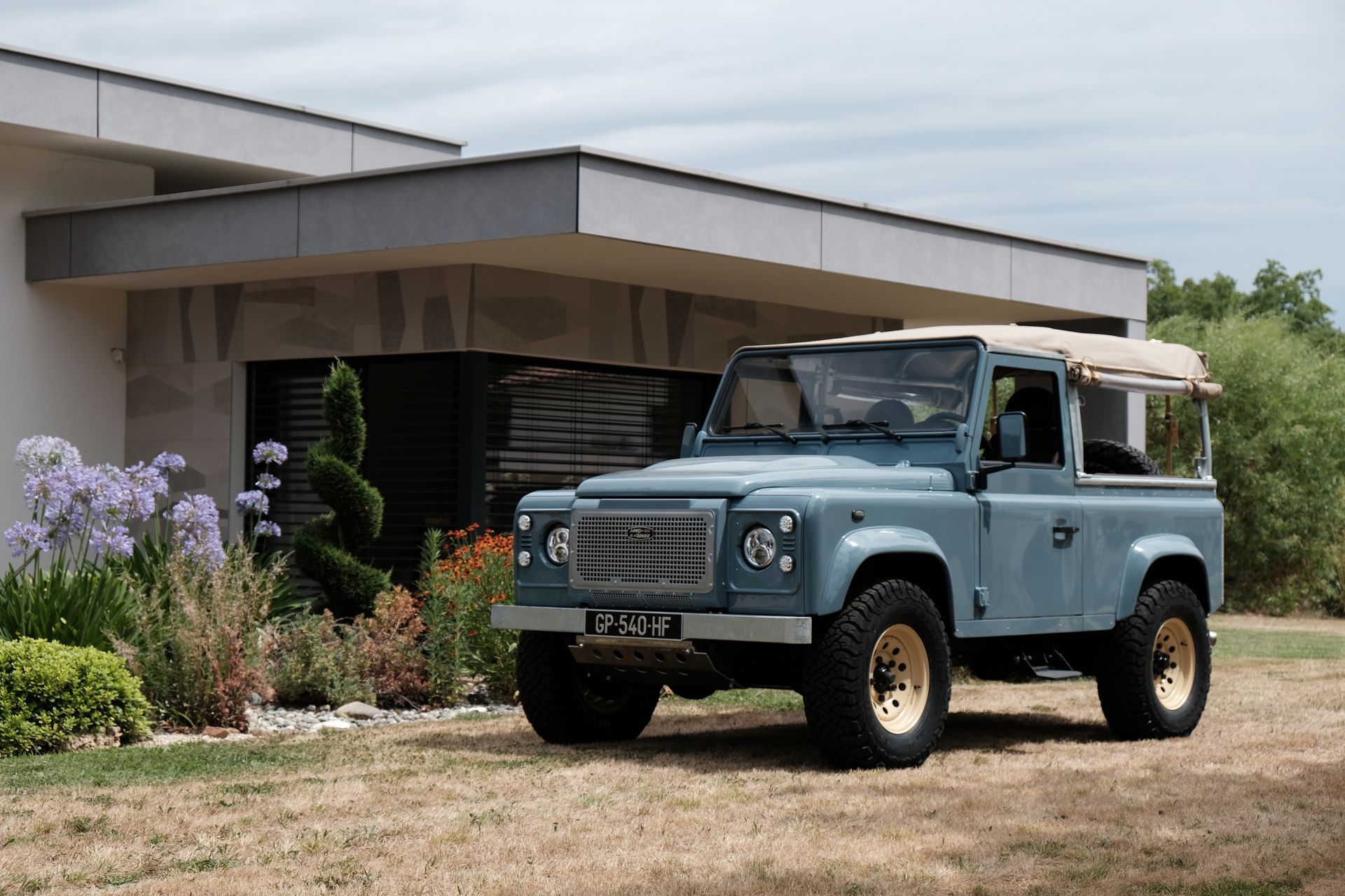 Un Land Rover Defender bleu est garé près d'un bâtiment moderne au toit beige.