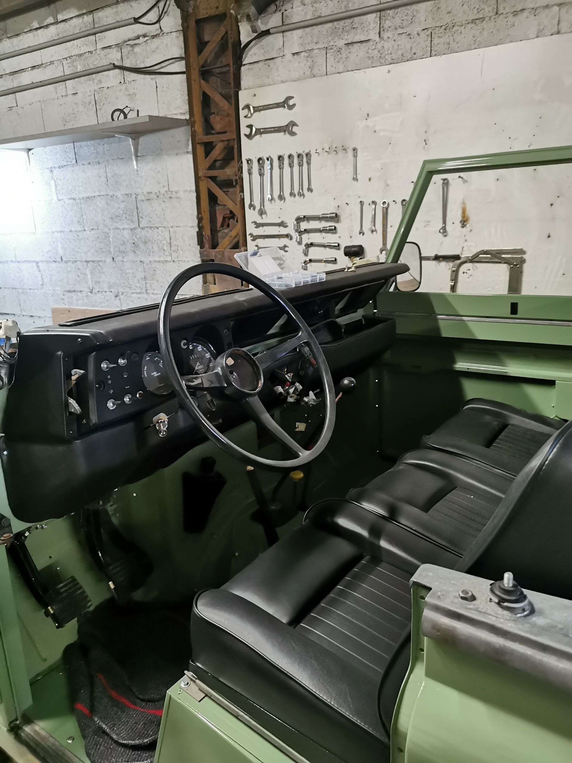 Intérieur de Land Rover vert avec sièges et tableau de bord noirs, ambiance atelier.