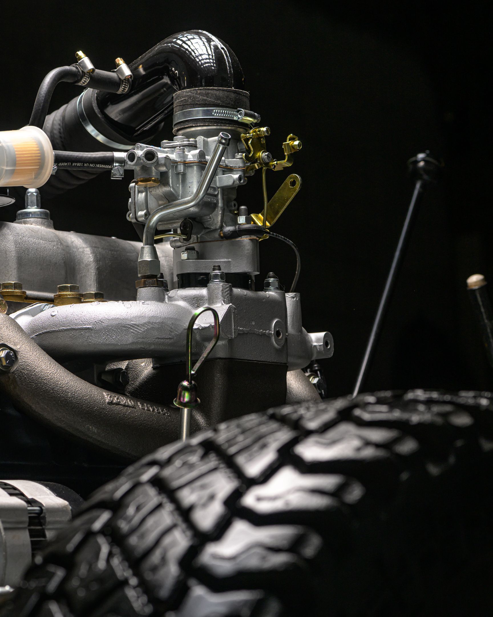 Gros plan sur le moteur et le pneu d'une voiture ancienne, sur fond sombre. Les détails du moteur apparaissent en argent.