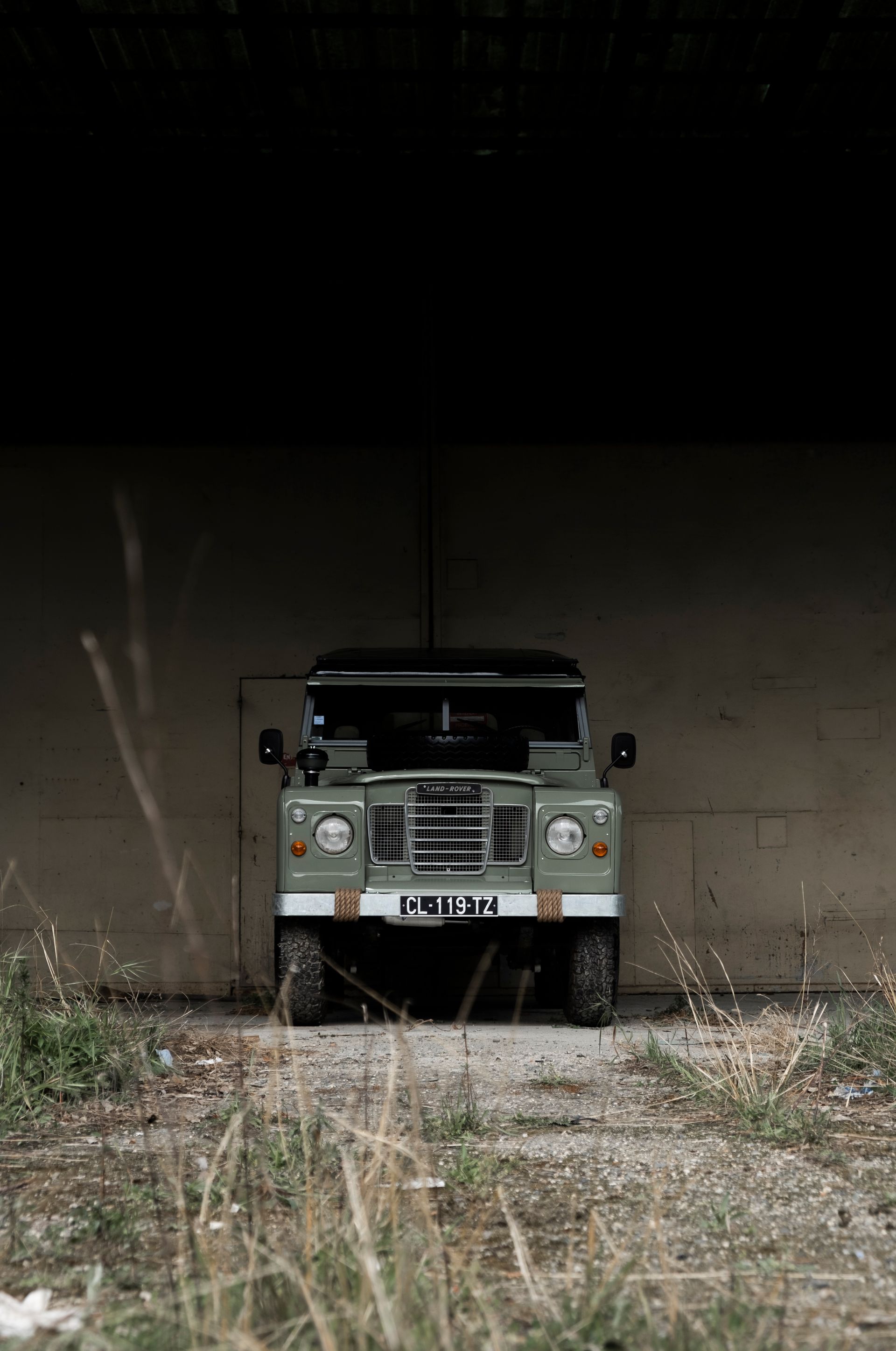 Un Land Rover Defender vert est stationné dans un tunnel sombre, face à la route.