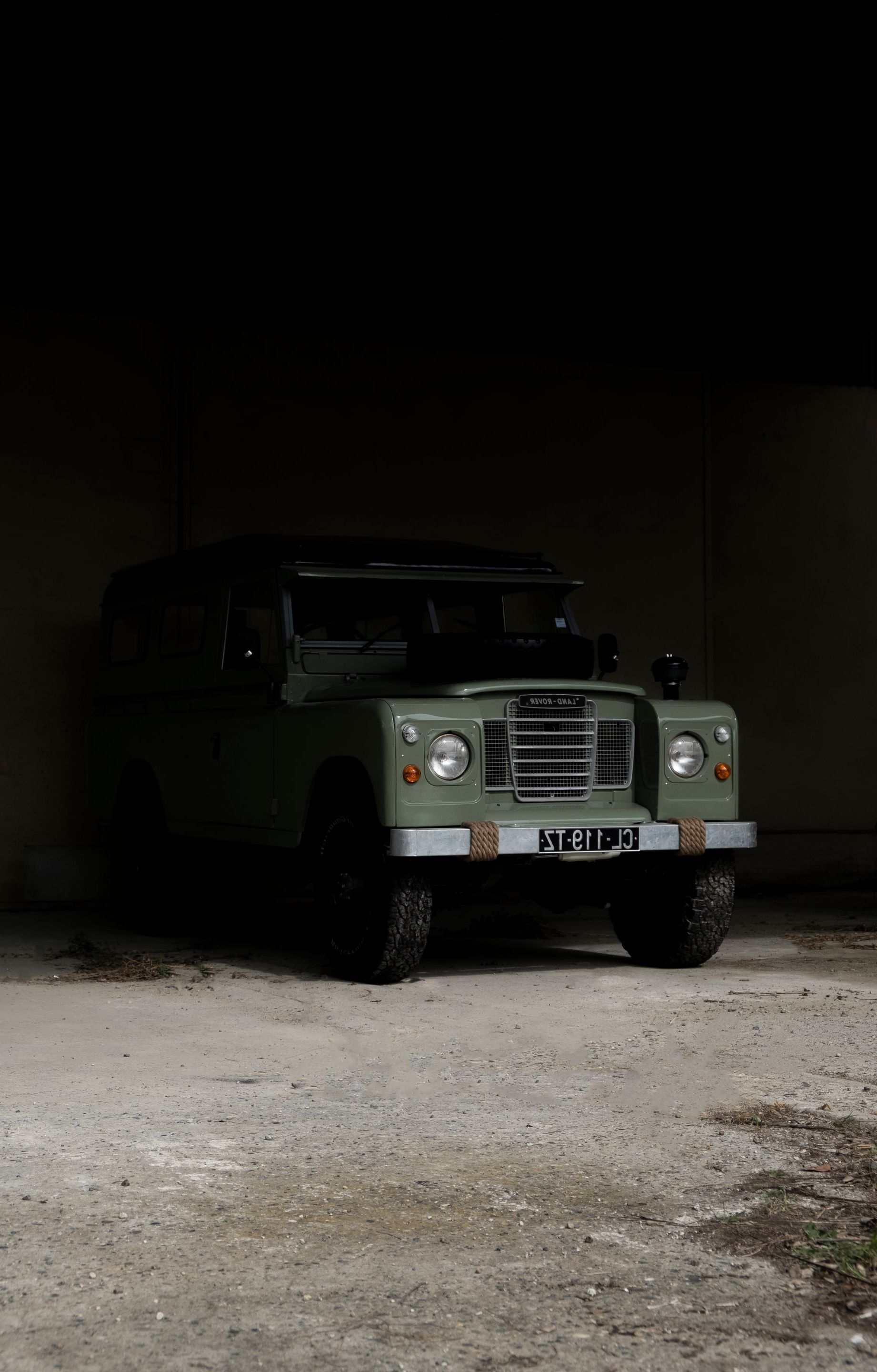 Un Land Rover vert est garé à l'intérieur d'un hangar sombre au sol en béton.