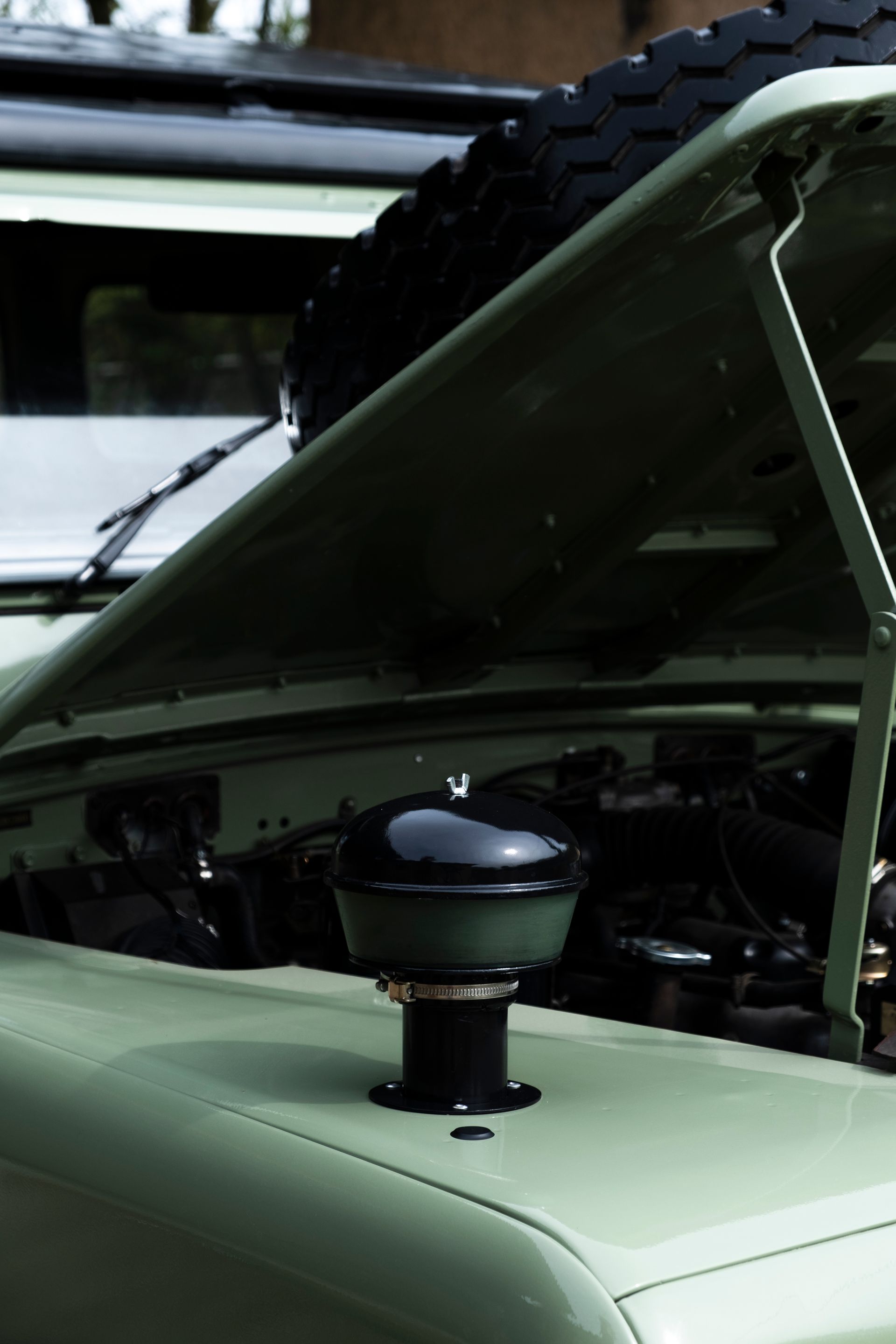 Land Rover vintage verte, capot ouvert, laissant apparaître un filtre à air noir.