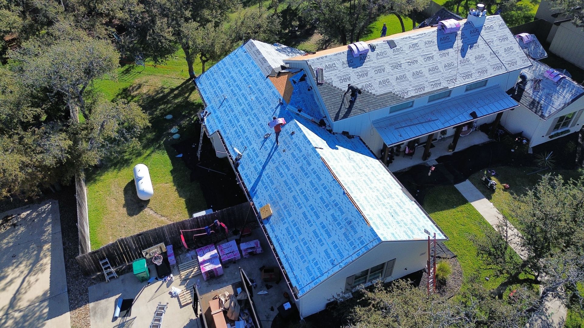 An aerial view of a house with a blue roof being installed.