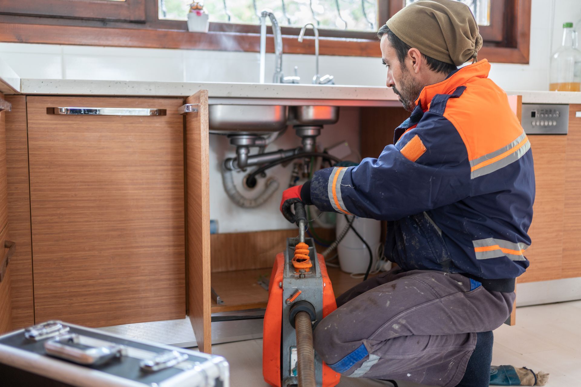 Person working under a kitchen sink with tools to fix or unclog plumbing pipes.
