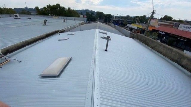 Metal roof with skylights and chimney, viewed from above, with buildings in the background.