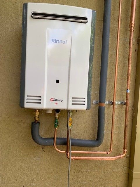 Rinnai tankless water heater mounted on a beige wall, with copper pipes and gray exhaust.