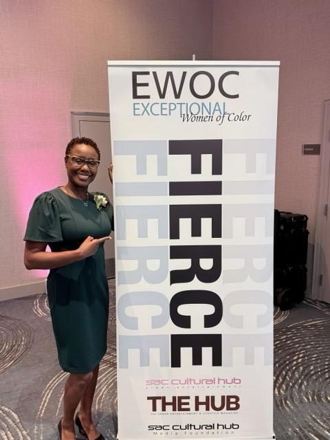 Woman in green dress posing beside an EWOC banner with “THE HUB” and “FIERCE” text.