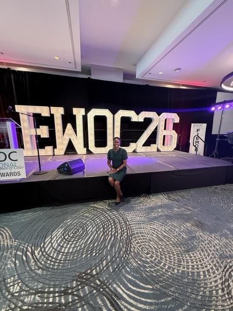 Person seated in front of a purple-lit stage with large “EWOC26” letters at an awards event