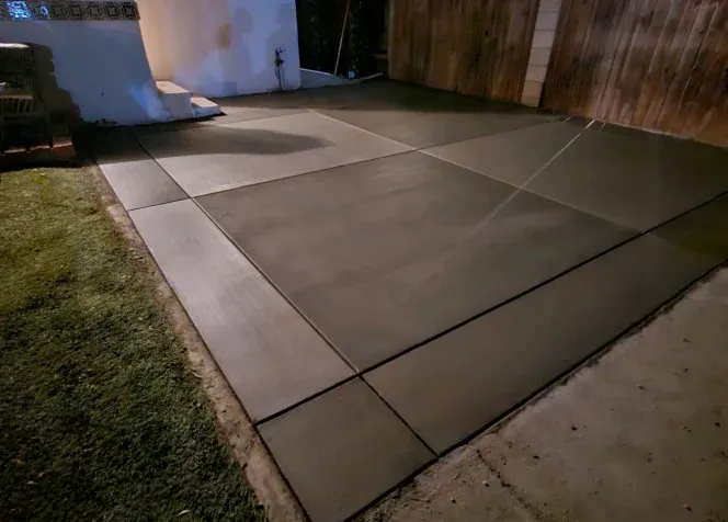 Freshly paved concrete patio beside a lawn and wooden fence at dusk