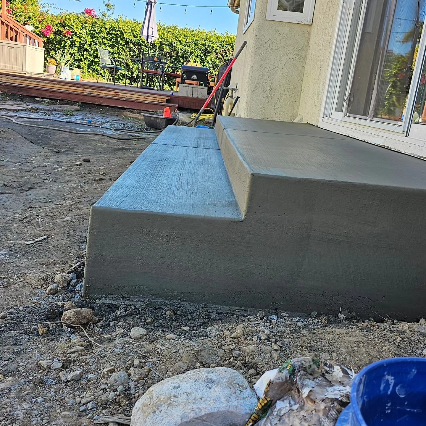 Fresh gray concrete step beside a stucco house, with gravel and a garden in the yard.