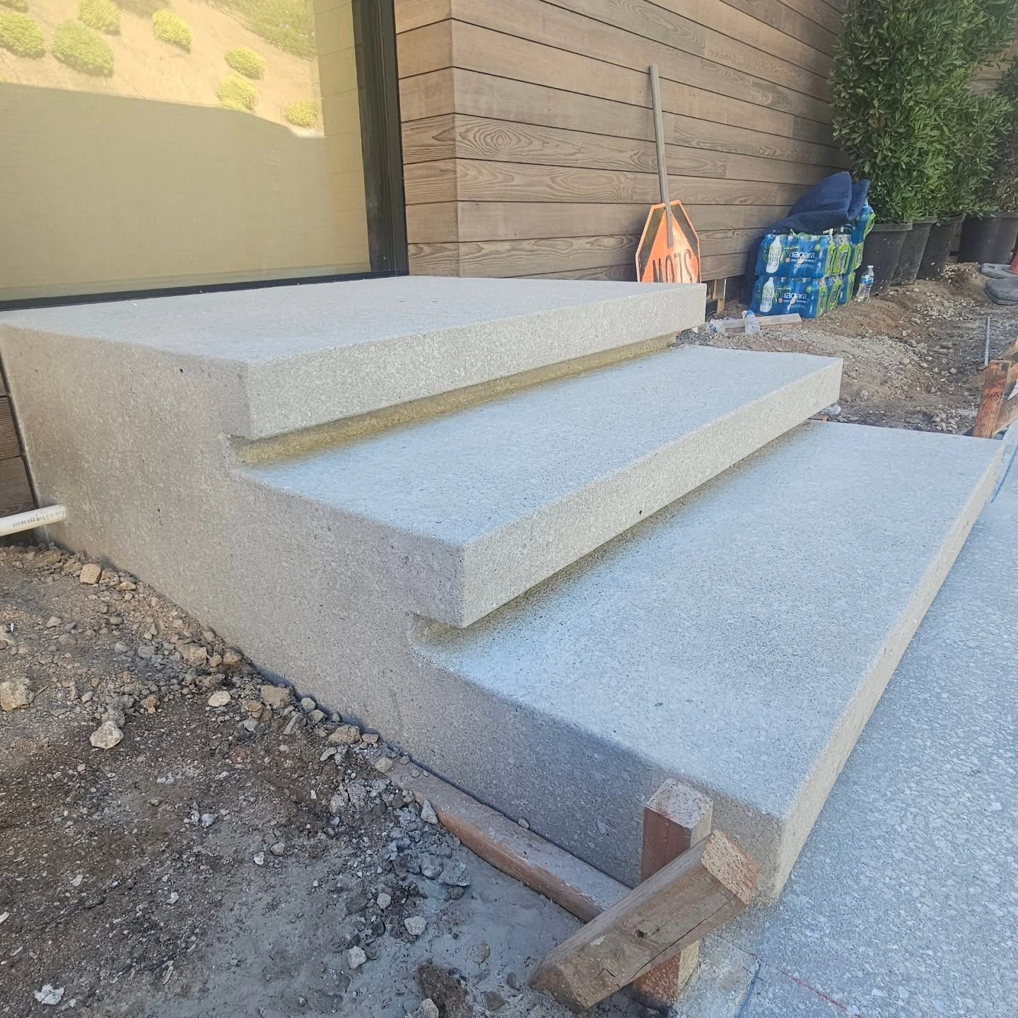 Concrete front steps under construction beside a house, with gravel and tools nearby.