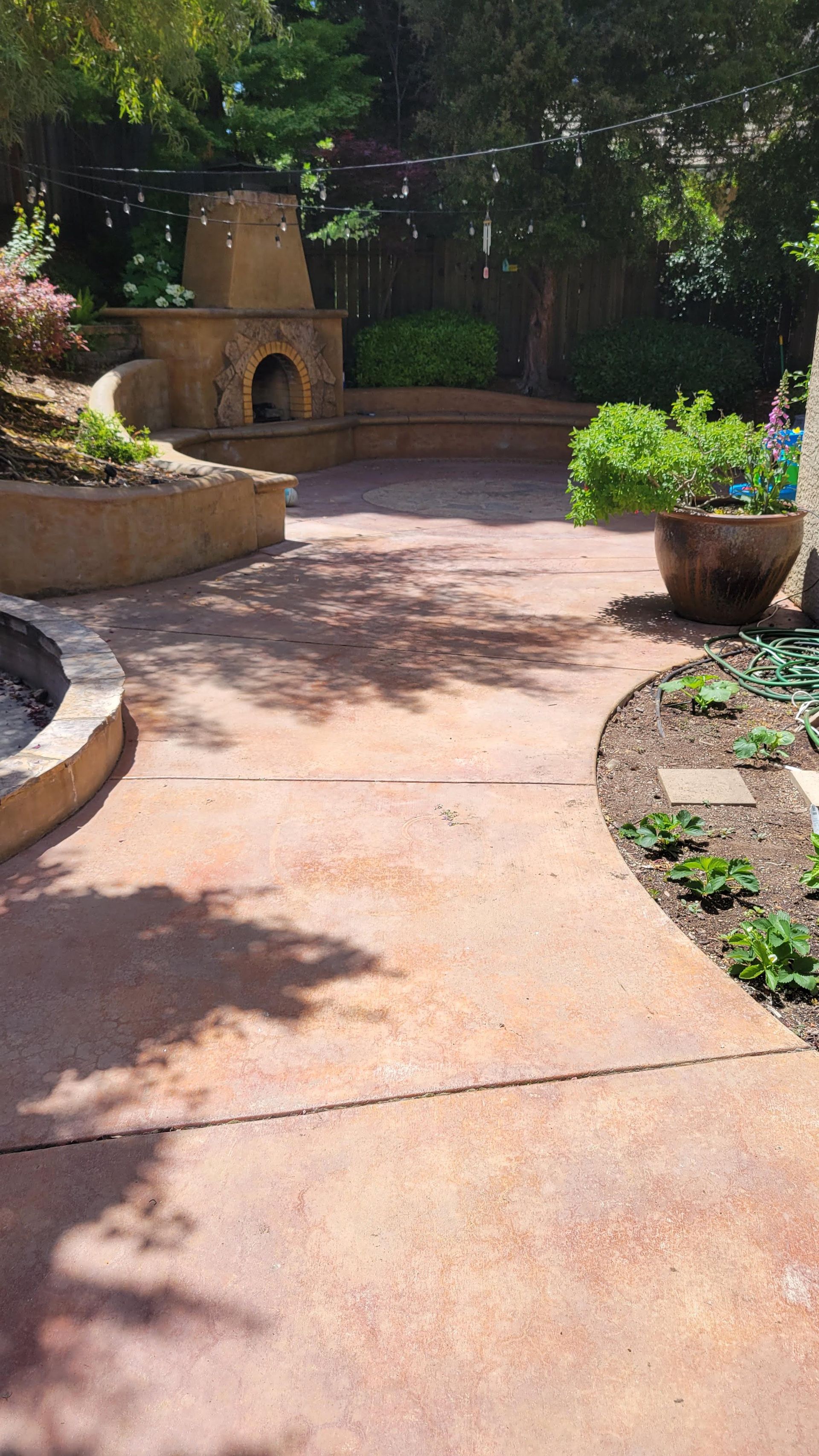 Curved sunlit garden path with stone planters and a small outdoor fireplace at the end