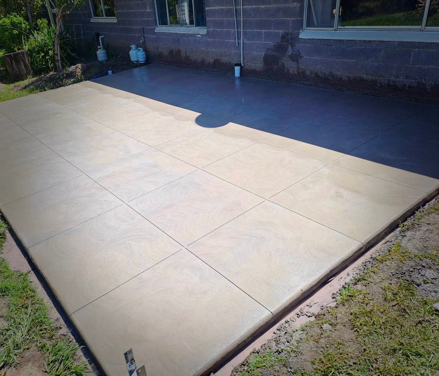Freshly poured concrete patio beside a brick house with a small step and surrounding grass