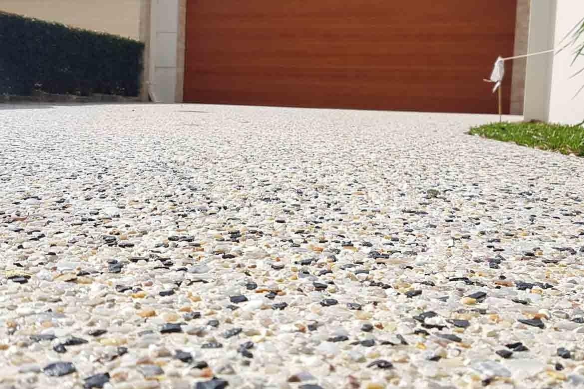 Low-angle view of a pebbled concrete driveway leading to a red garage door and a small patch of grass.