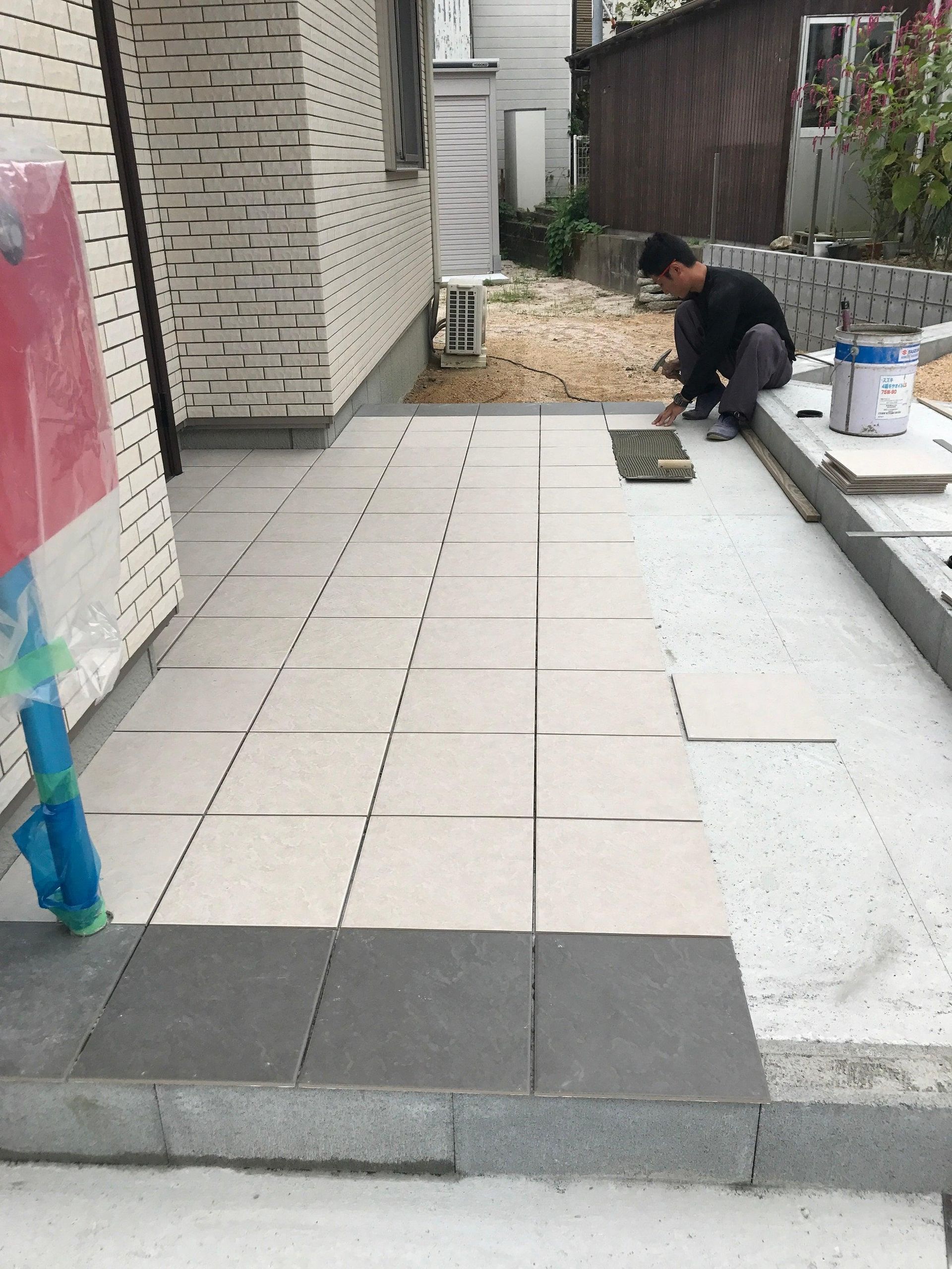 Worker laying paving stones in a narrow outdoor courtyard beside a brick wall