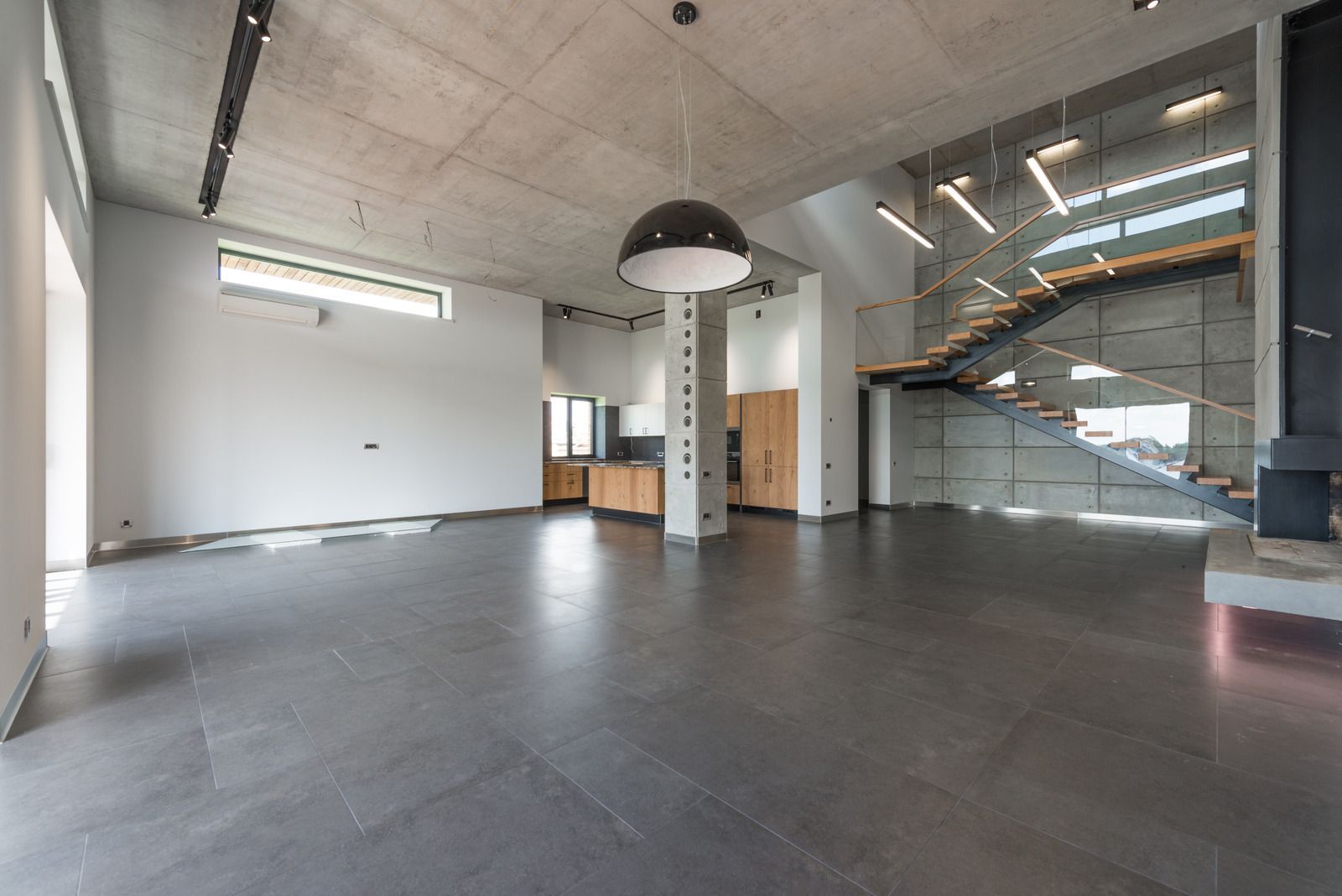 Empty modern loft space with polished concrete floors, exposed ceiling, and a staircase by large windows