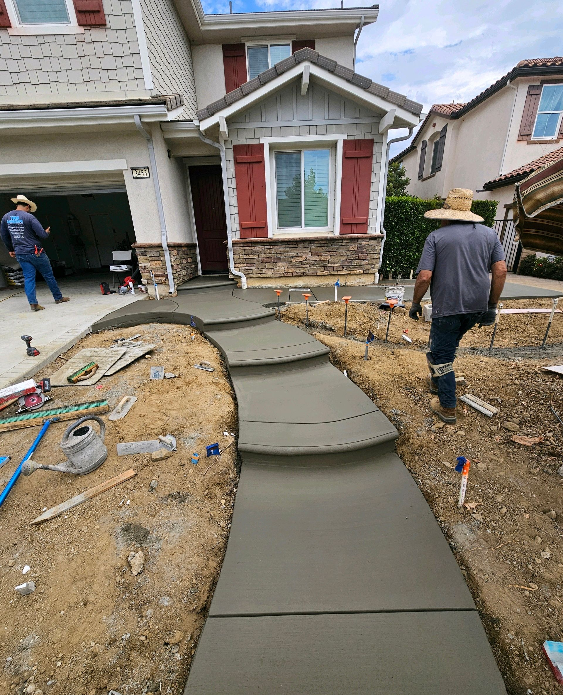Front yard with new concrete walkway leading to a house, with two workers nearby and a garage open.