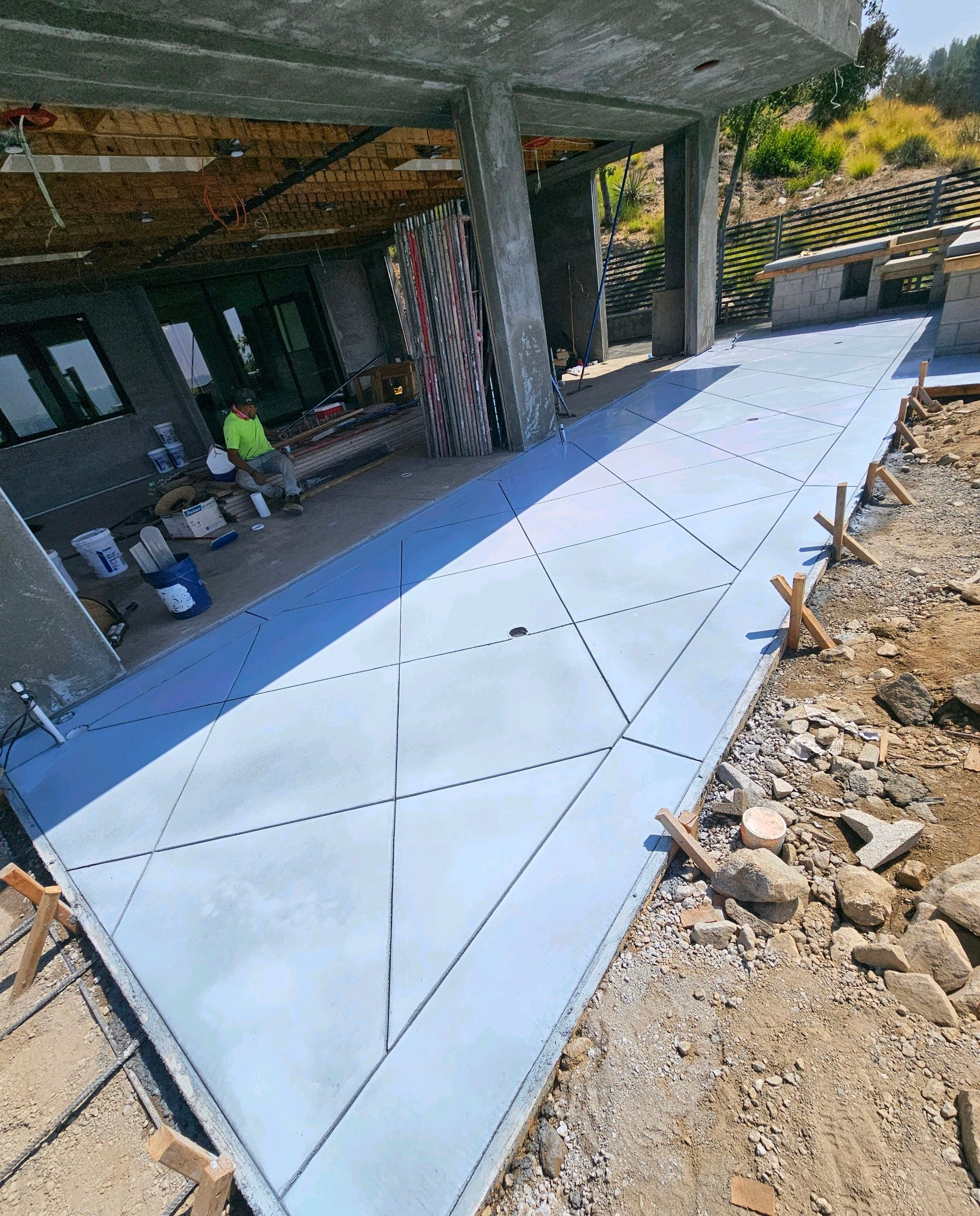 Concrete patio under construction beside a house, with white triangular panels and surrounding dirt.