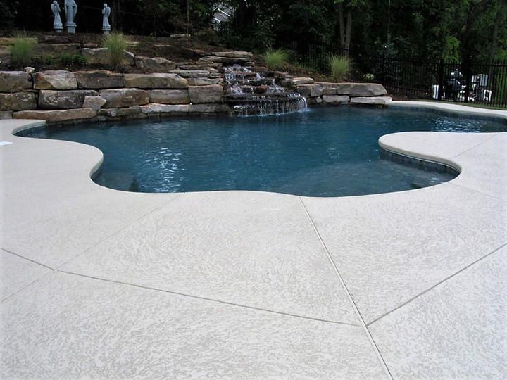 Curved backyard pool with stone waterfall and light-colored patio decking