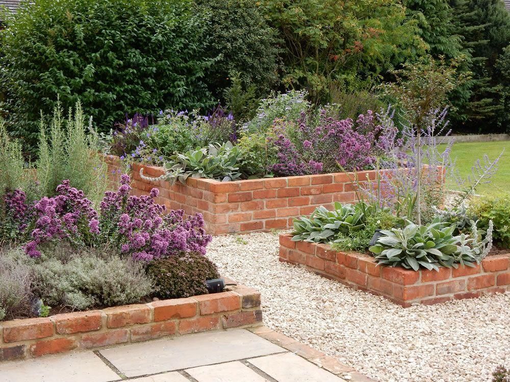 Brick garden beds with purple flowers and green plants along a gravel path