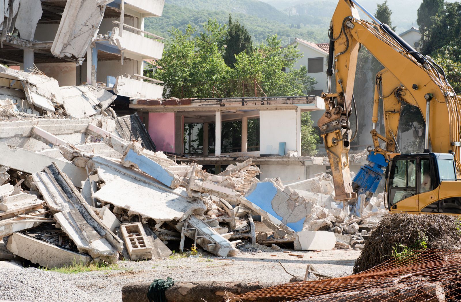 Demolition excavator clearing rubble from a collapsed building in a residential area