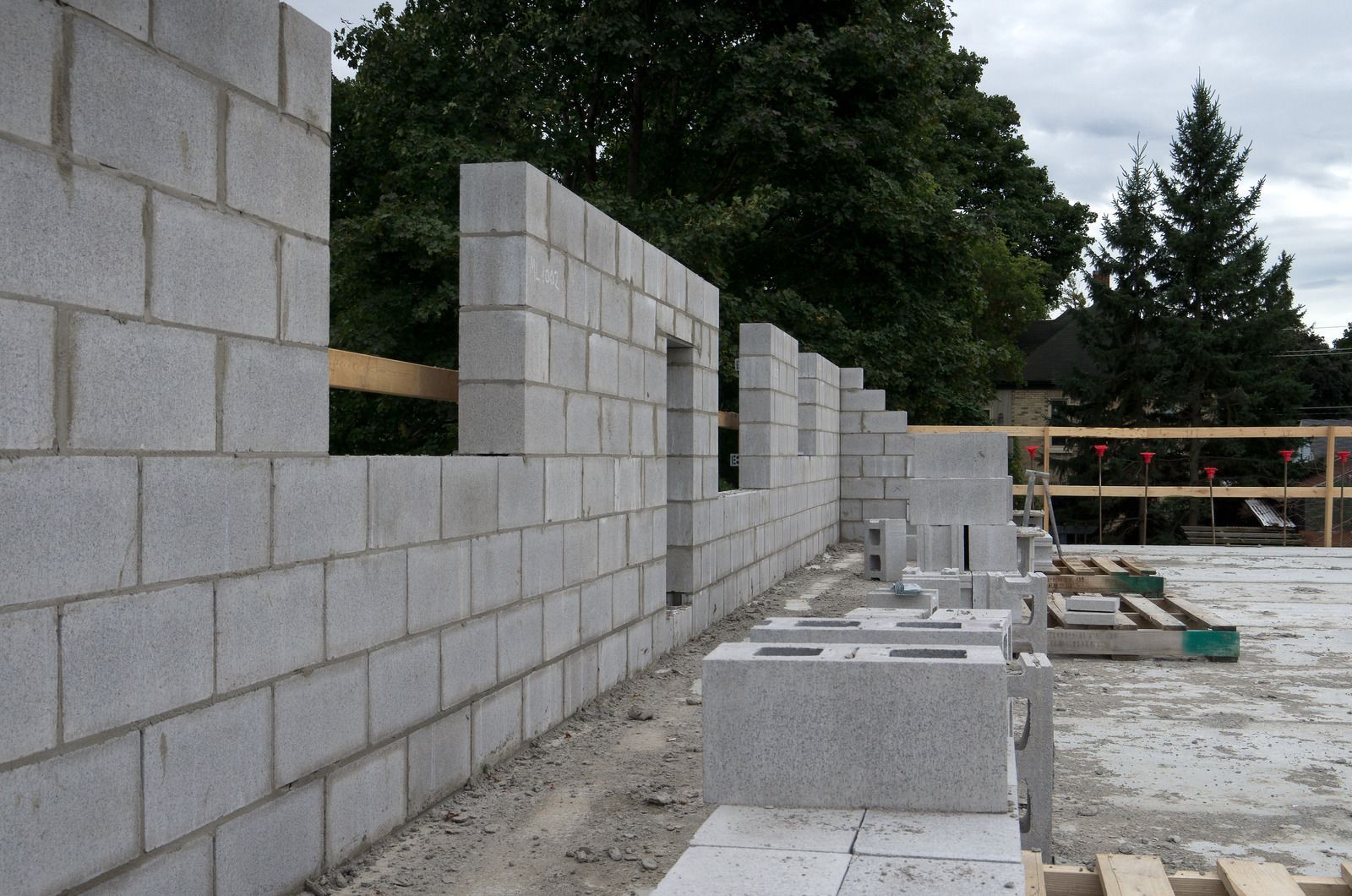 Partially built cinder block wall at a construction site with stacked blocks and trees in the background