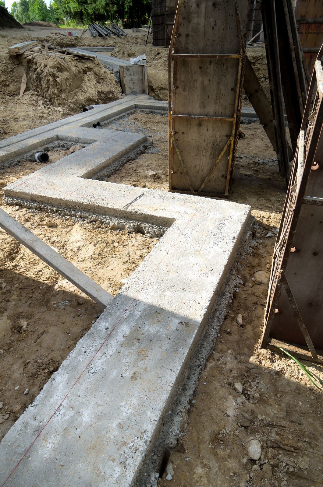 Concrete foundation footings and trench beside a large vertical wooden support post on a construction site