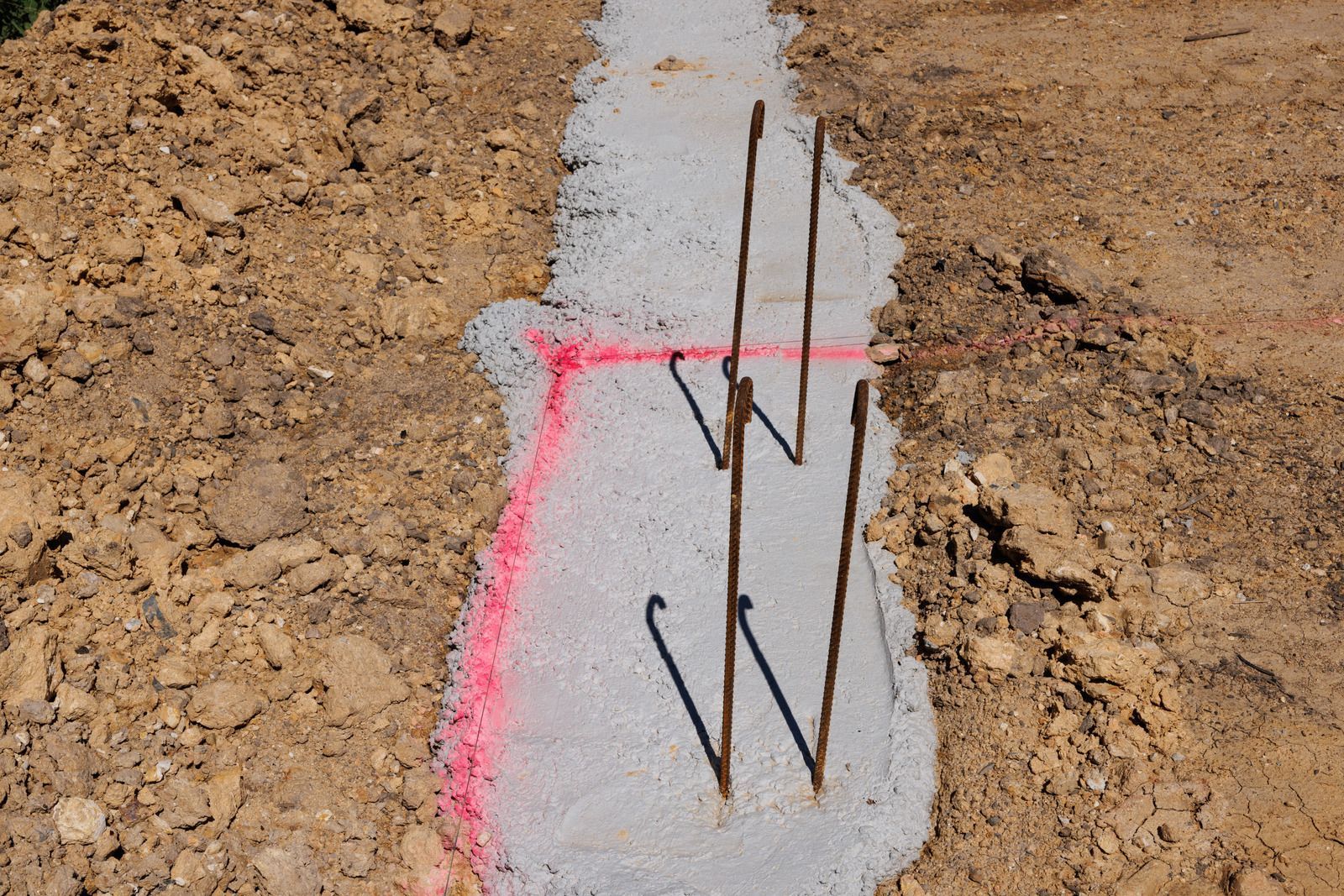 Concrete footing with exposed rebar marked by pink spray paint in dirt soil