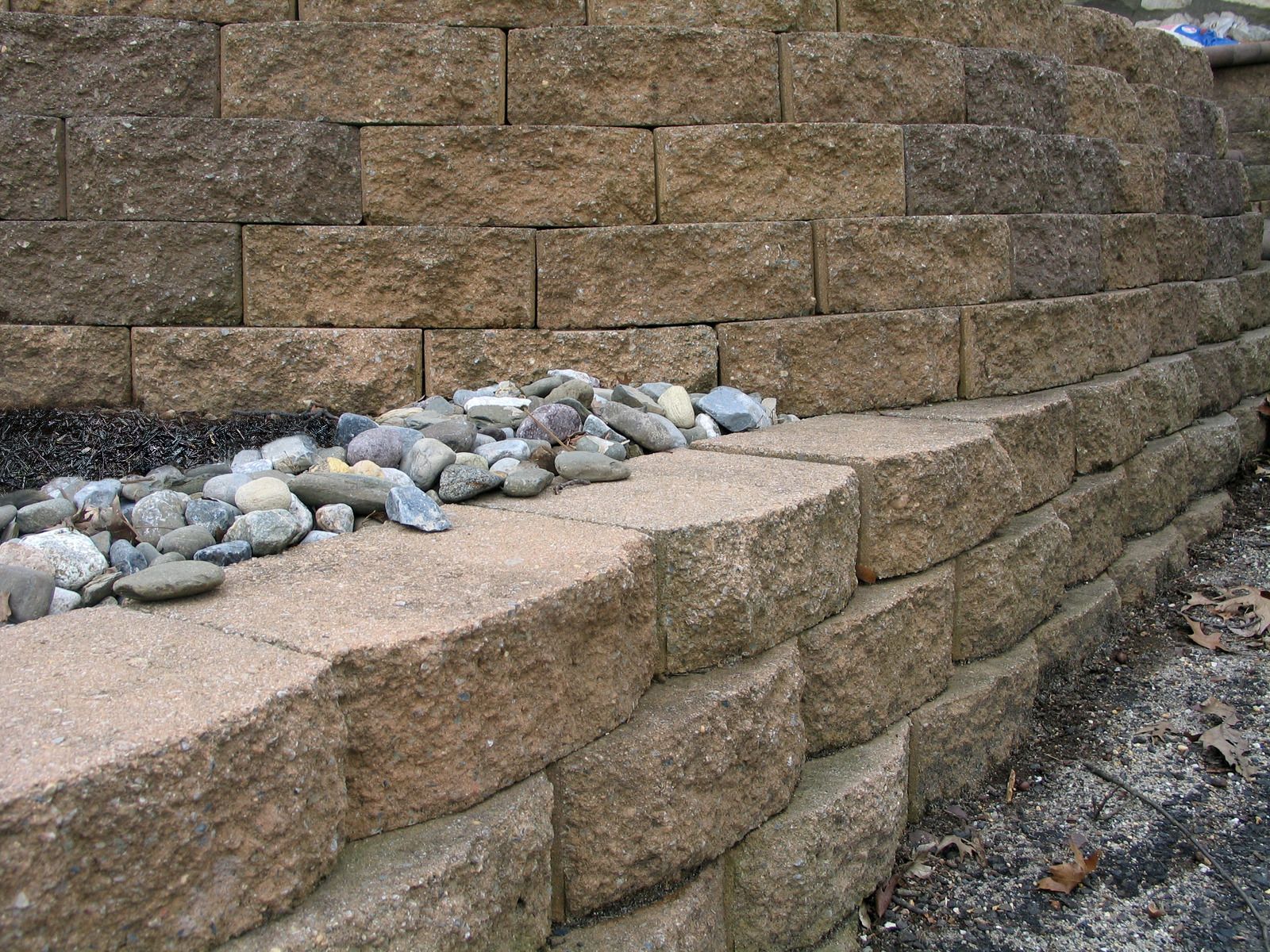 Stone retaining wall with a narrow ledge topped by small rocks and gravel below