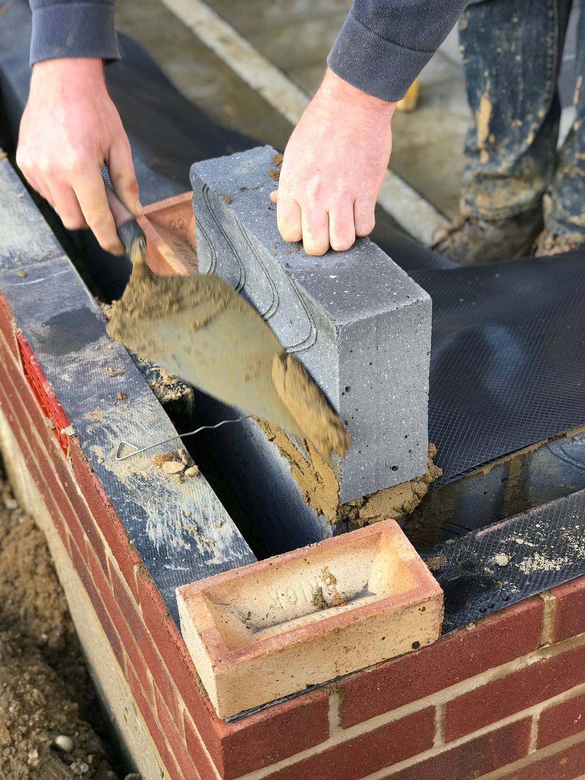 Hands troweling wet mortar onto a cinder block wall under construction