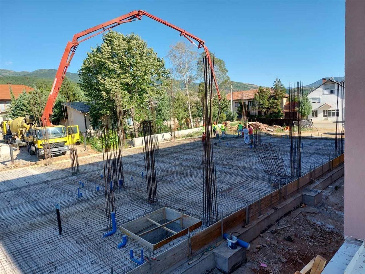 Concrete foundation pour with workers and a red boom pump at a residential construction site.