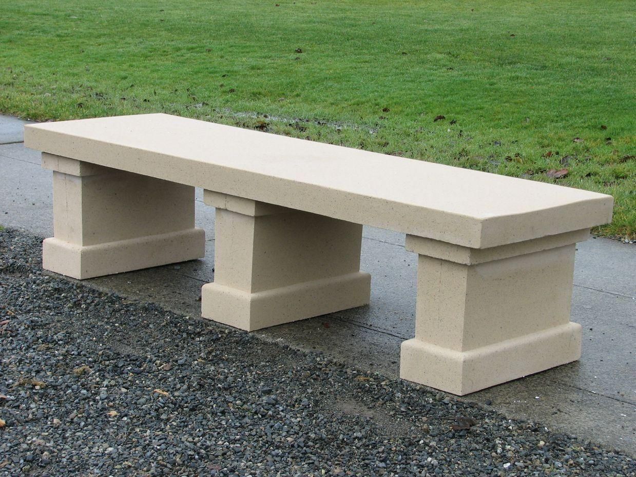 Concrete park bench on gravel beside a grassy lawn