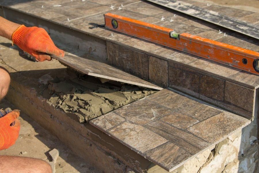 Gloved worker troweling mortar into a stone-tile walkway beside a level and straightedge