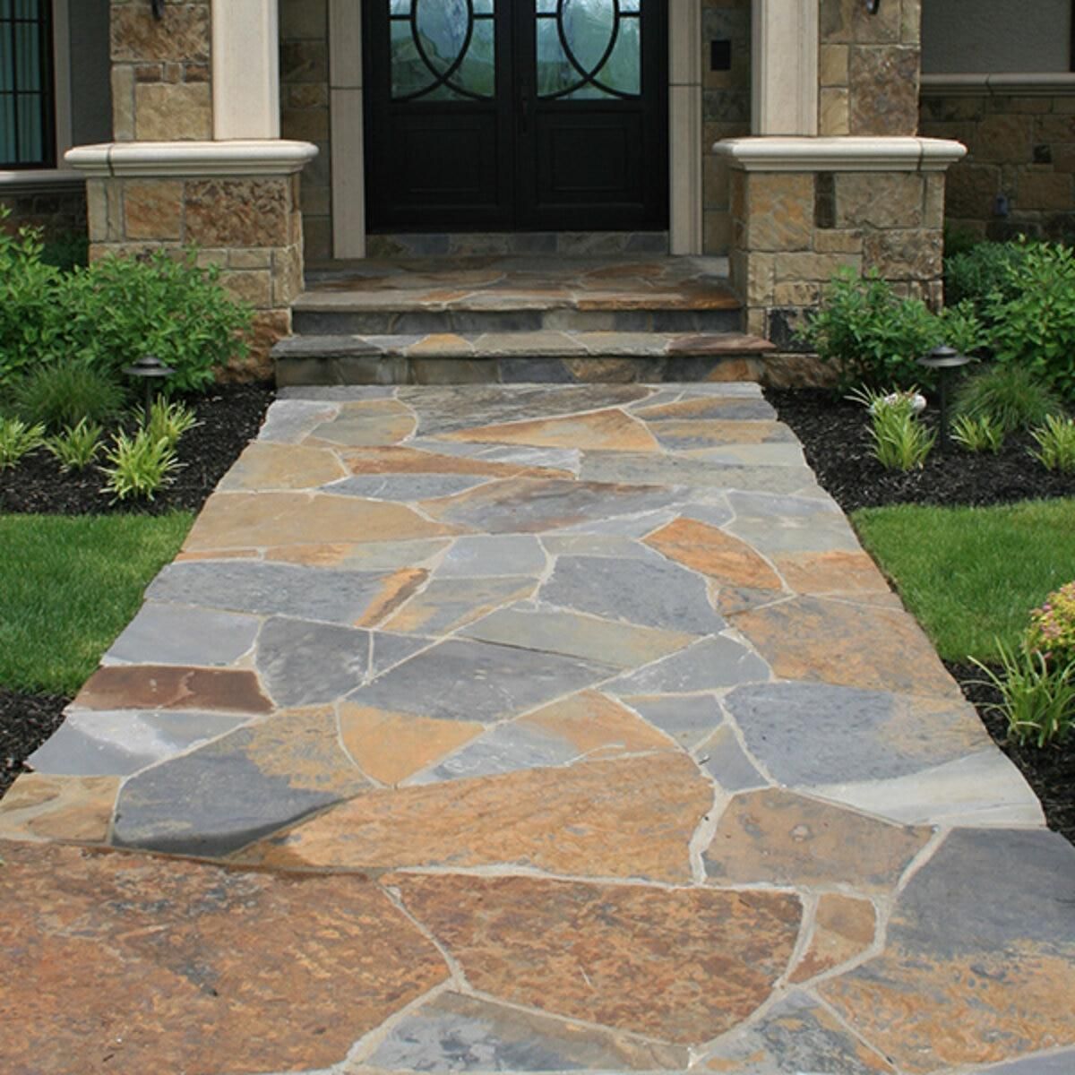 Stone walkway leading to a front door, bordered by grass and landscaping